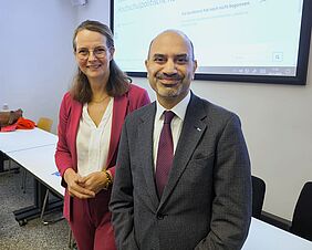 Ministerin Bettina Martin und DAAD-Präsident Prof. Dr. Joybrato Mukherjee lächeln in die Kamera. Im Hintergrund ist ein beleuchtetes Smartboard zu sehen.